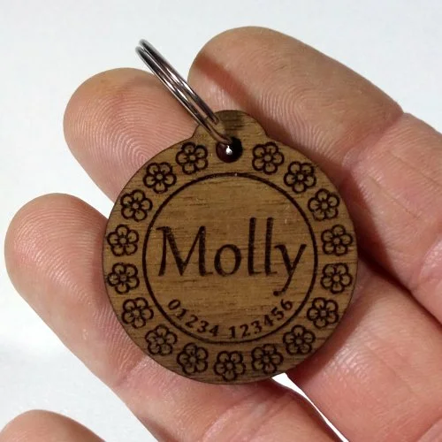 Wooden pet tag with engraved name 'Molly' and phone number, decorated with a flower border