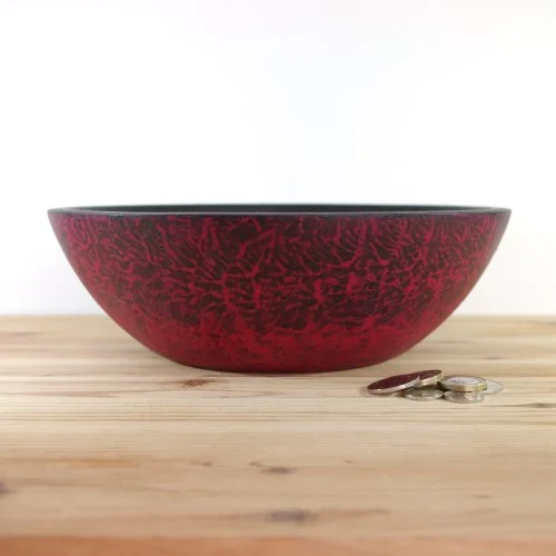 A red and black bowl on a wooden surface with a few coins next to it.