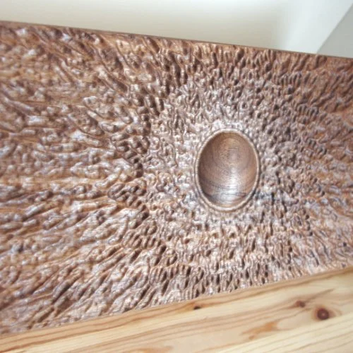 Close-up of a textured wooden surface with a circular indentation in the center.