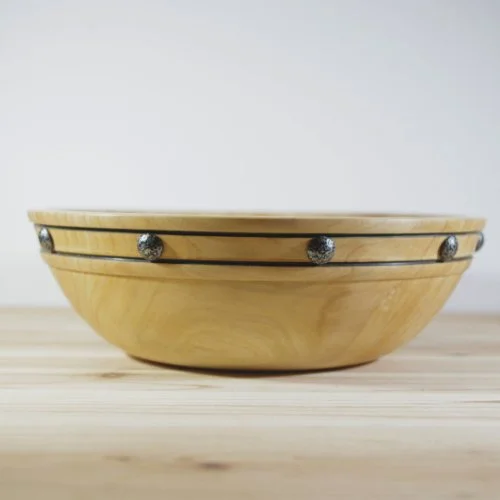 Wooden bowl with decorative black and silver accents on a light wooden surface.