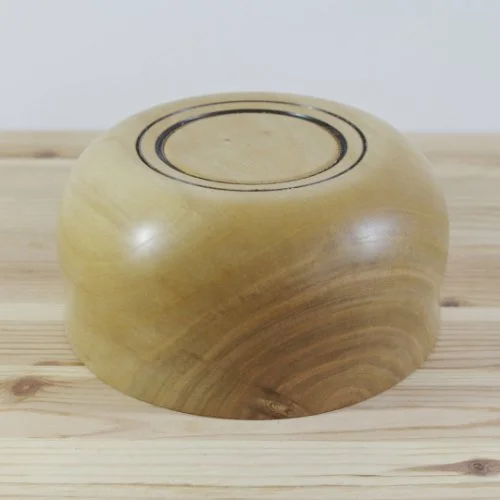 A light-colored wooden bowl placed upside down on a wooden surface.