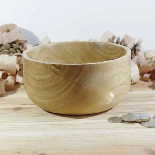 Wooden bowl placed on a wooden surface with scattered coins and small rocks in background.