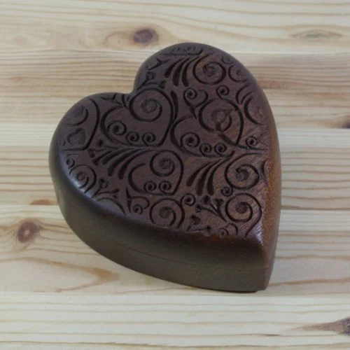 A dark chocolate heart-shaped box with intricate swirl and spiral patterns on top, placed on a wooden surface.
