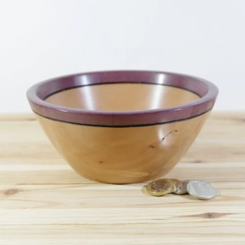steamed pear wooden bowl with a purple heart rim on a wooden surface, with three coins in front of it.