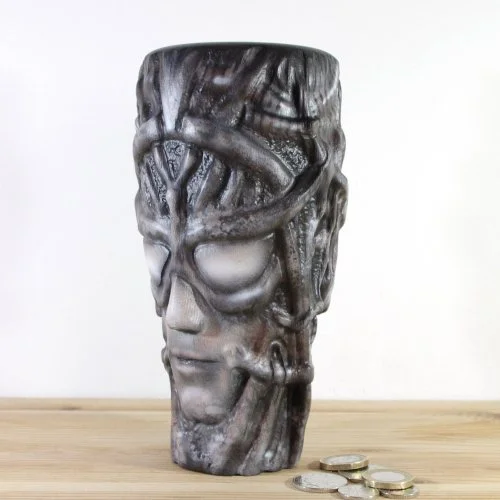 A wooden vase inspired by H.R.Giger with face design, placed on a wooden surface with coins in front.