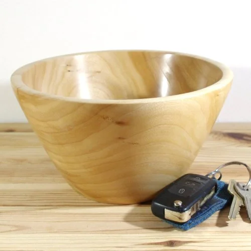 A polished wooden bowl with car keys and a key fob on a wooden surface.