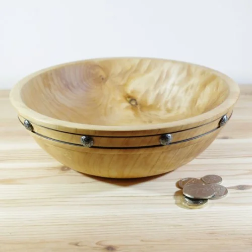 A wooden salad bowl with metal accents sitting on a wooden surface next to a few coins.