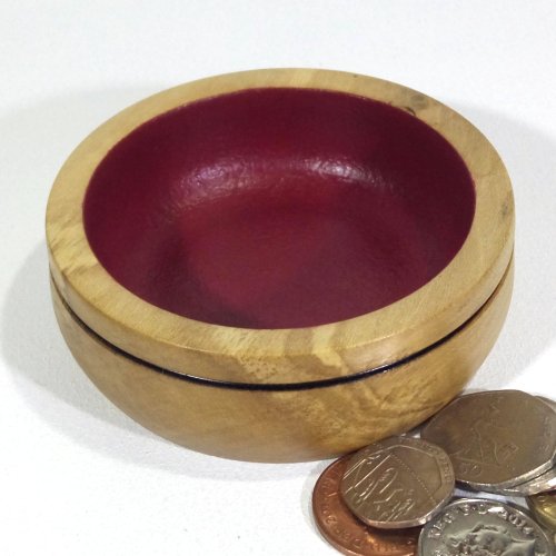 A small wooden bowl with a red interior, placed next to a few coins on a white surface.