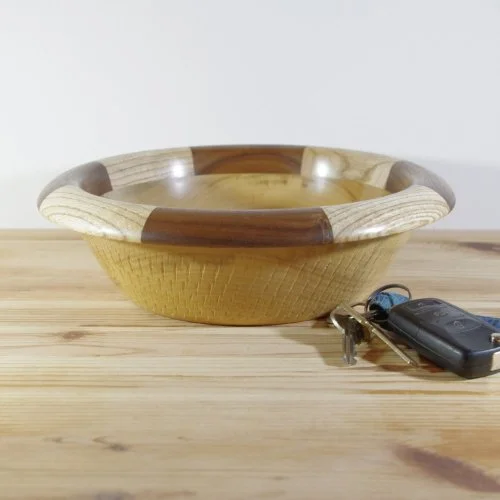 A wooden bowl with a gold-colored interior sitting on a wooden table next to car keys.