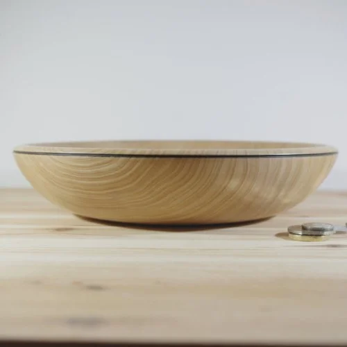 A wooden bowl on a light wooden surface with some coins beside it, against a plain background.