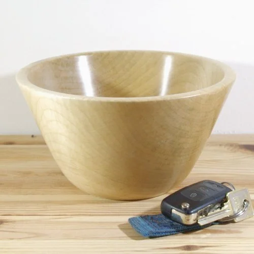Light-colored wooden bowl sitting on a wooden surface with a car key and keychain next to it