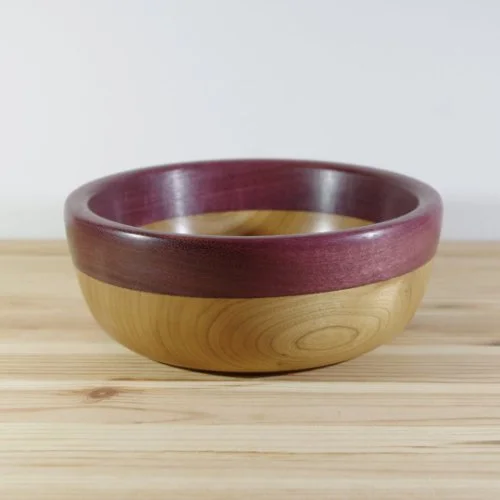 A wooden bowl with a natural wood color inside and a dark purple or maroon exterior, placed on a light wooden surface.