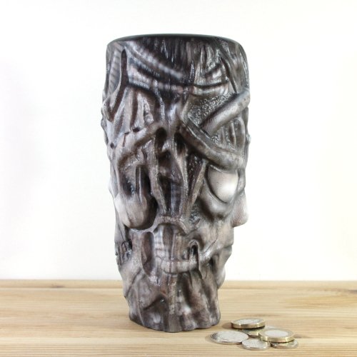 A wooden vase inspired by H.R.Giger, placed on a wooden surface with a few coins in front of it.