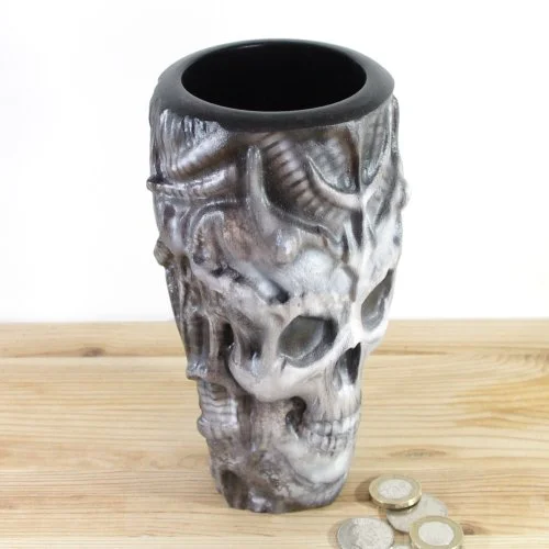 A wooden vase inspired by H.R.Giger, placed on a wooden surface next to some coins.