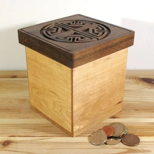 A wooden keepsake box with a decorative engraved top, placed on a wooden surface with coins in front.