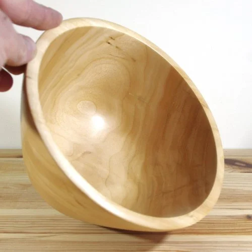 A hand holding a wooden bowl on a wooden surface.