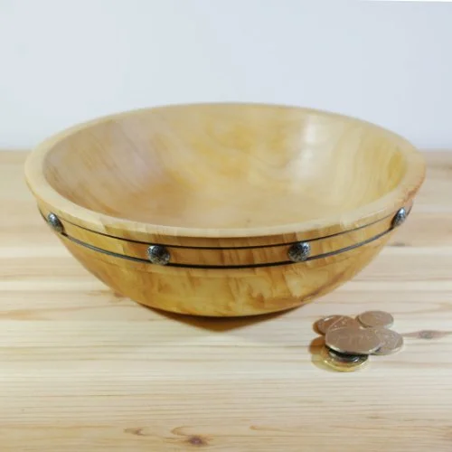 Wooden bowl with metal accents placed on a wooden surface next to some coins.