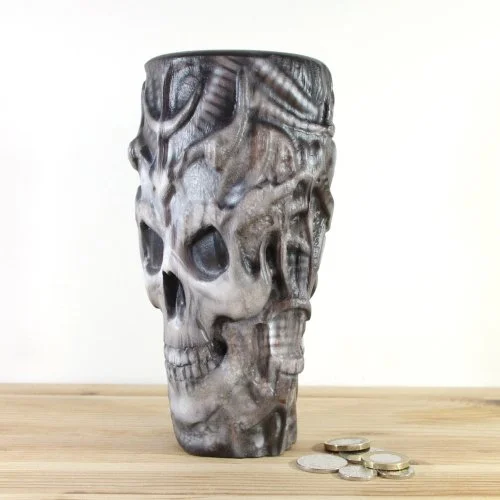 A wooden skull vase inspired by H.R.Giger, placed on a wooden surface next to some coins.