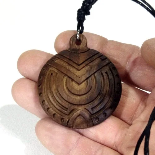 Round wooden pendant with engraved geometric patterns, attached to a black cord.