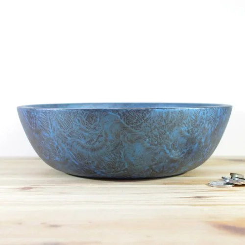 A large blue wooden bowl with a marbled pattern on a wooden surface next to a few coins.