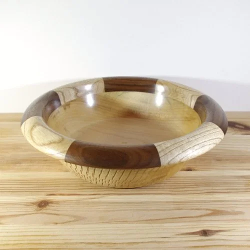 A wooden bowl with a two-tone design on a light wood surface.