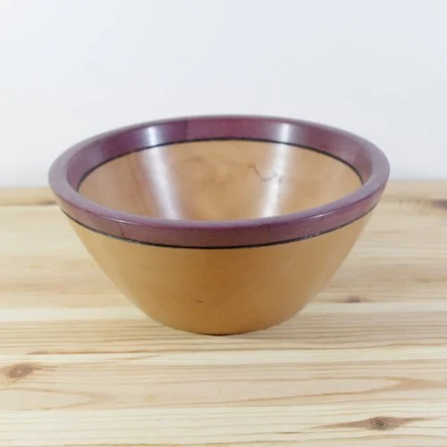 Wooden bowl with a purple rim on a light wooden surface.