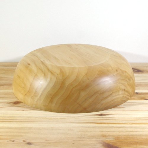 A smooth, polished wooden bowl on a wooden surface against a white background.