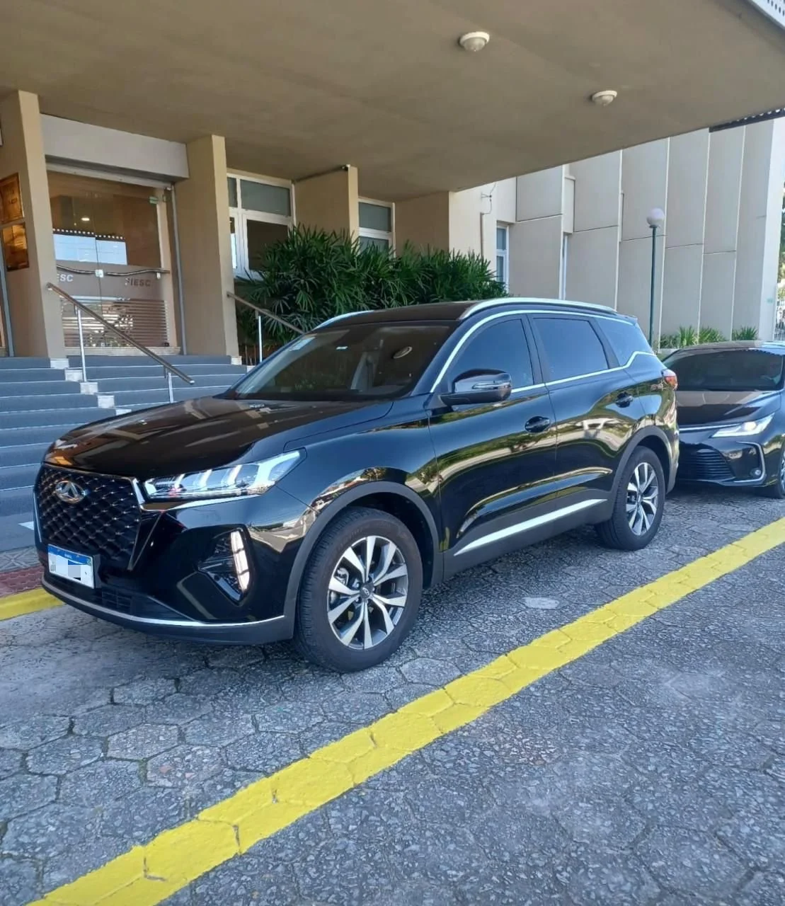 Carro preto estacionado em frente à entrada de um prédio, ao lado de outro veículo