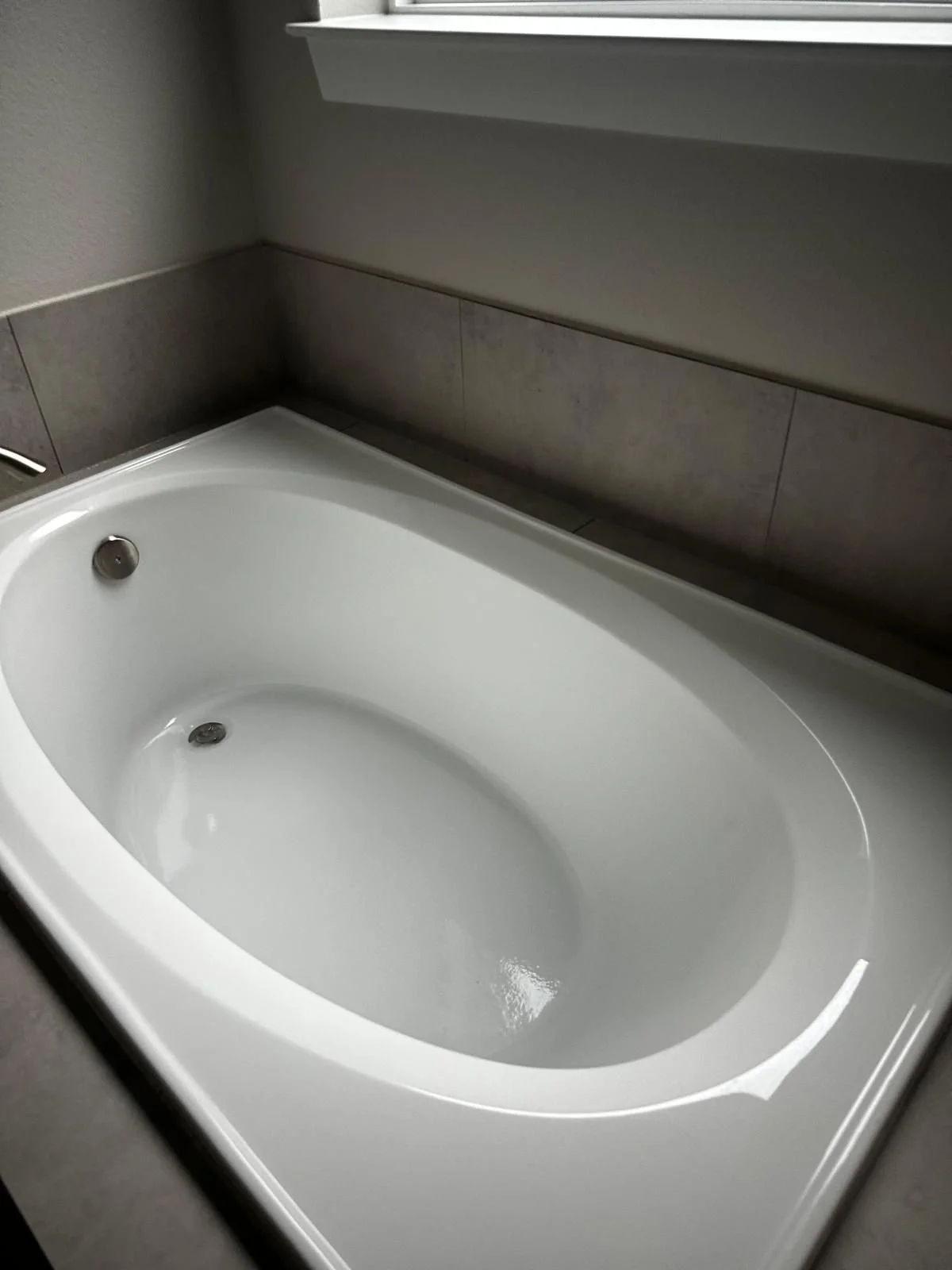 Empty white bathtub in a bathroom with gray tile walls and a small ledge above it.