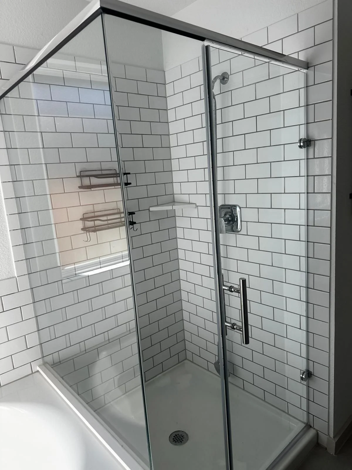 A modern glass shower enclosure with white subway tile walls and a chrome showerhead and handle.