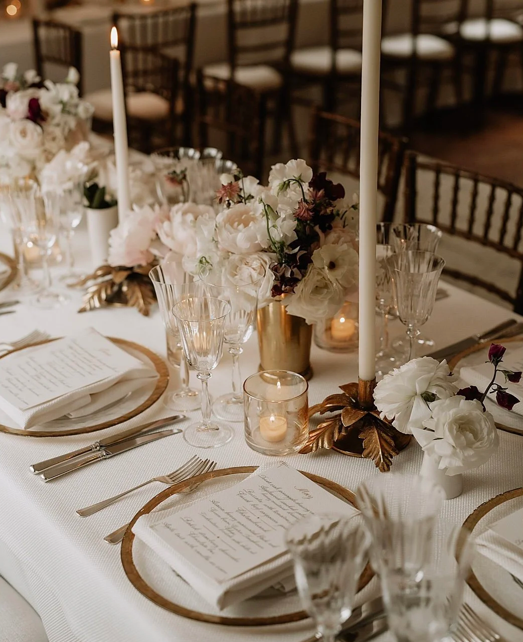 Elegant wedding table setting with white and blush flowers, tall candles, and soft lighting.