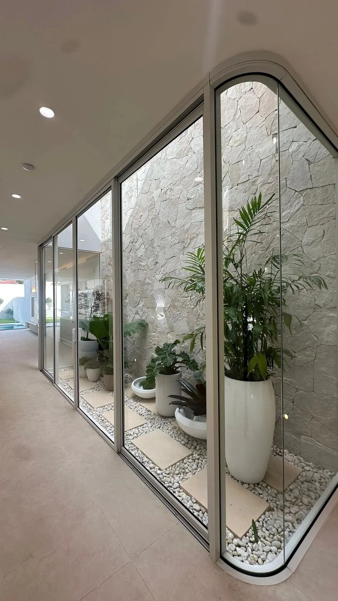 Indoor glass-enclosed plant display area with potted green plants and decorative white stones.