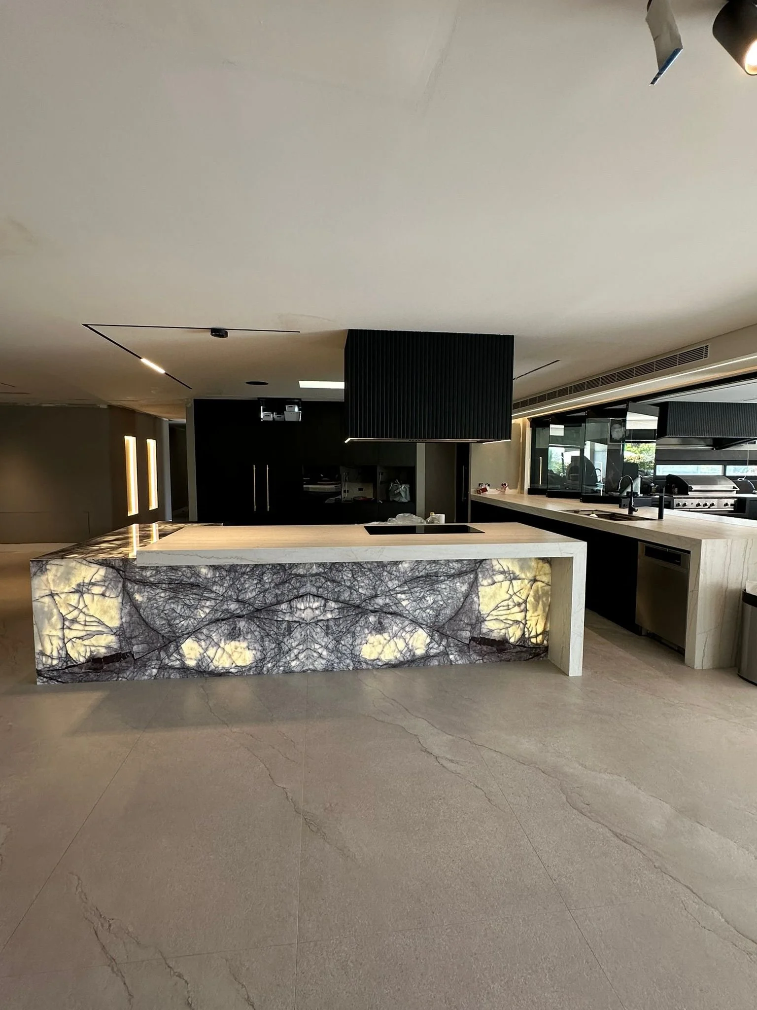 Modern kitchen with illuminated onyx island, black and white cabinetry, and large windows.