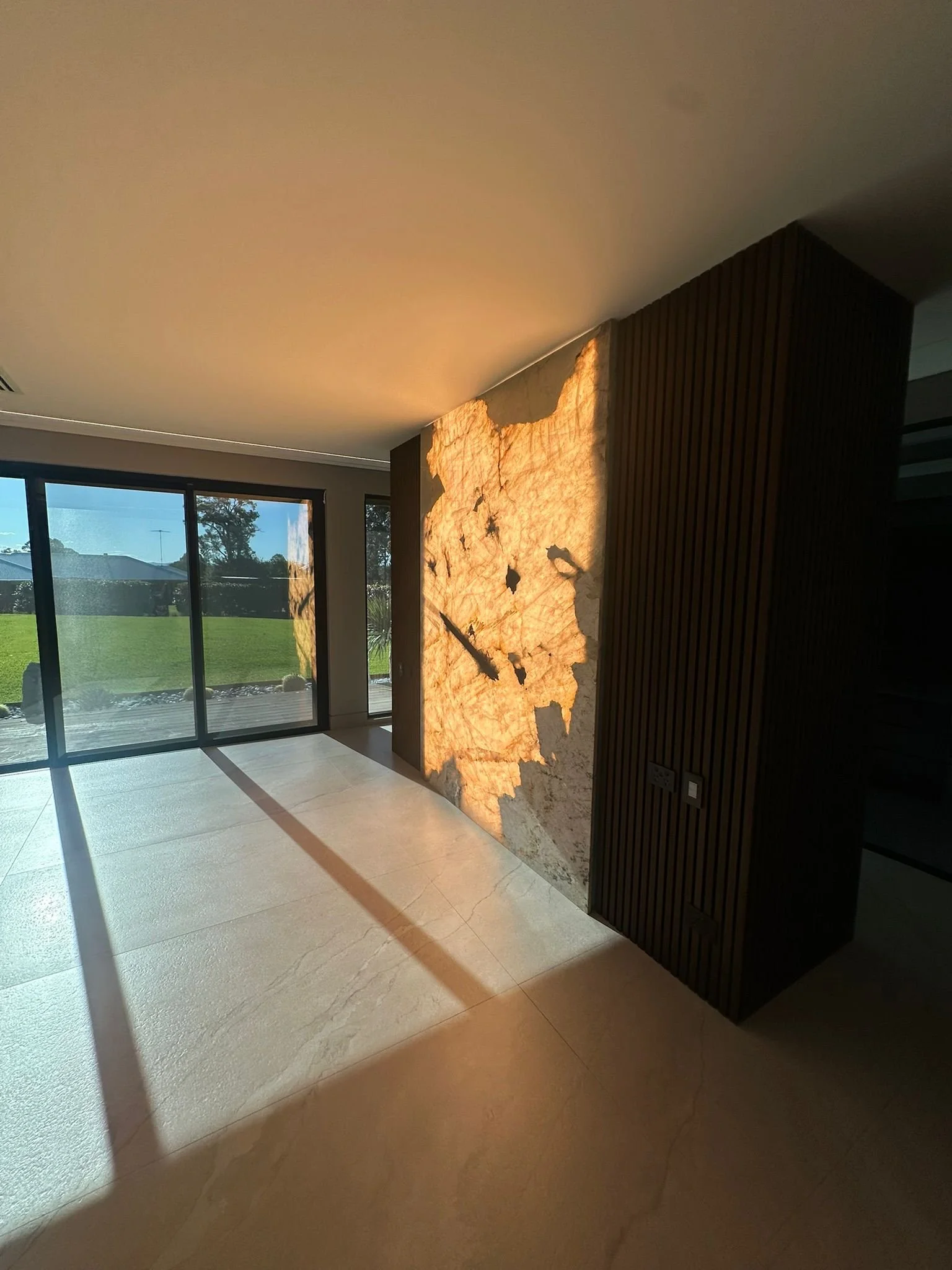 Modern interior with a decorative backlit wall feature resembling a map or abstract design, next to large glass sliding doors revealing a green outdoor space.