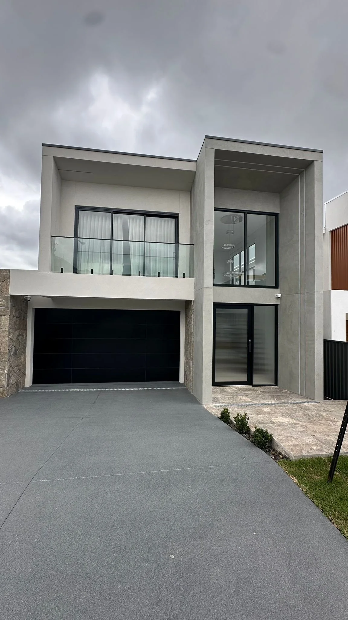 Modern two-story house with a black garage door, large windows, and a small front yard on a cloudy day.