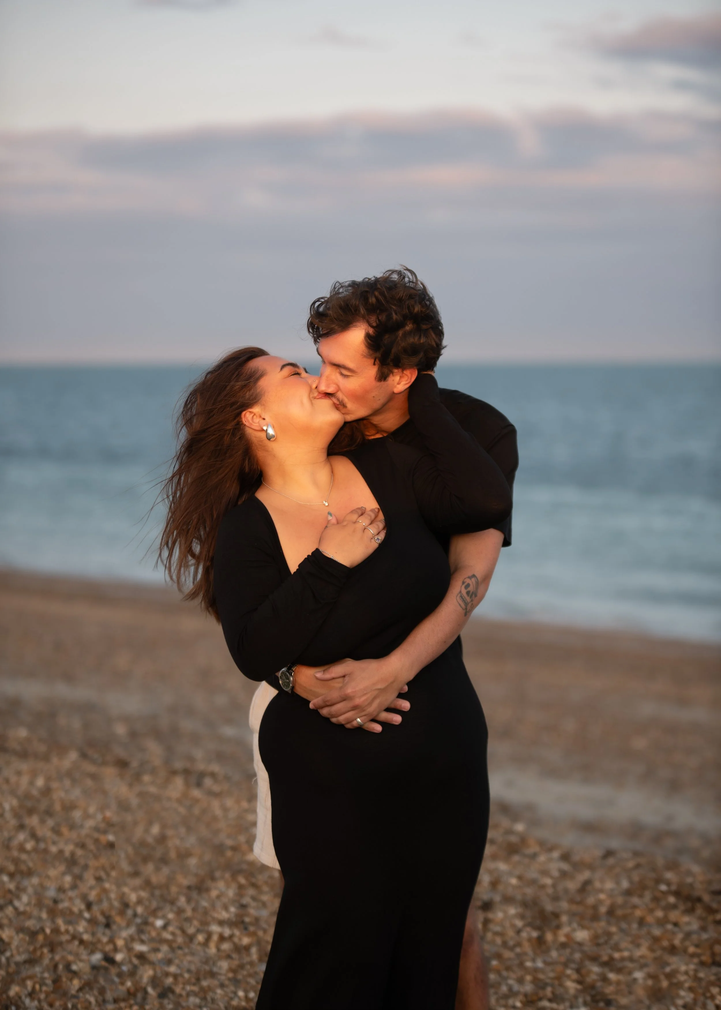 Couple kissing on beach; sea; pebbles; sunset; photography; engagement; ring