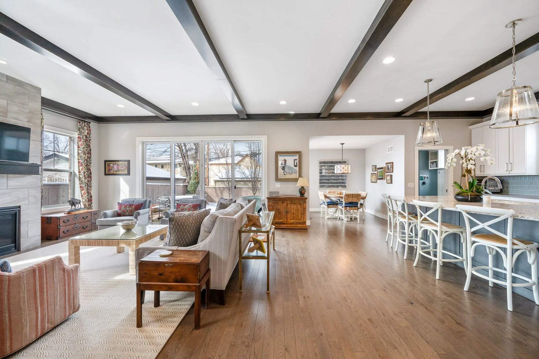 Family room and kitchen bar area with stone fireplace, wood floor and neutral tones 