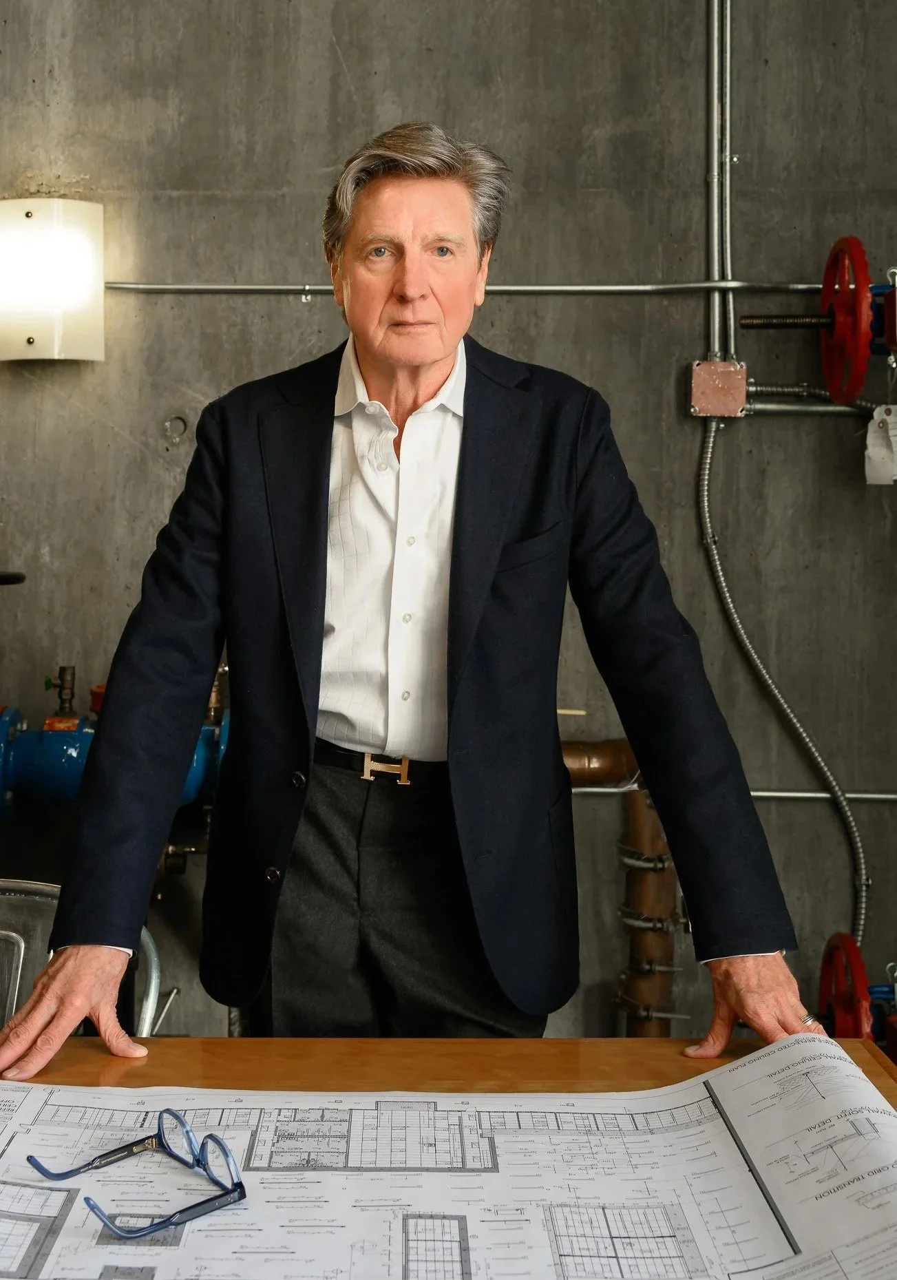 Executive man standing in front of architectural plans in office with concrete wall behind
