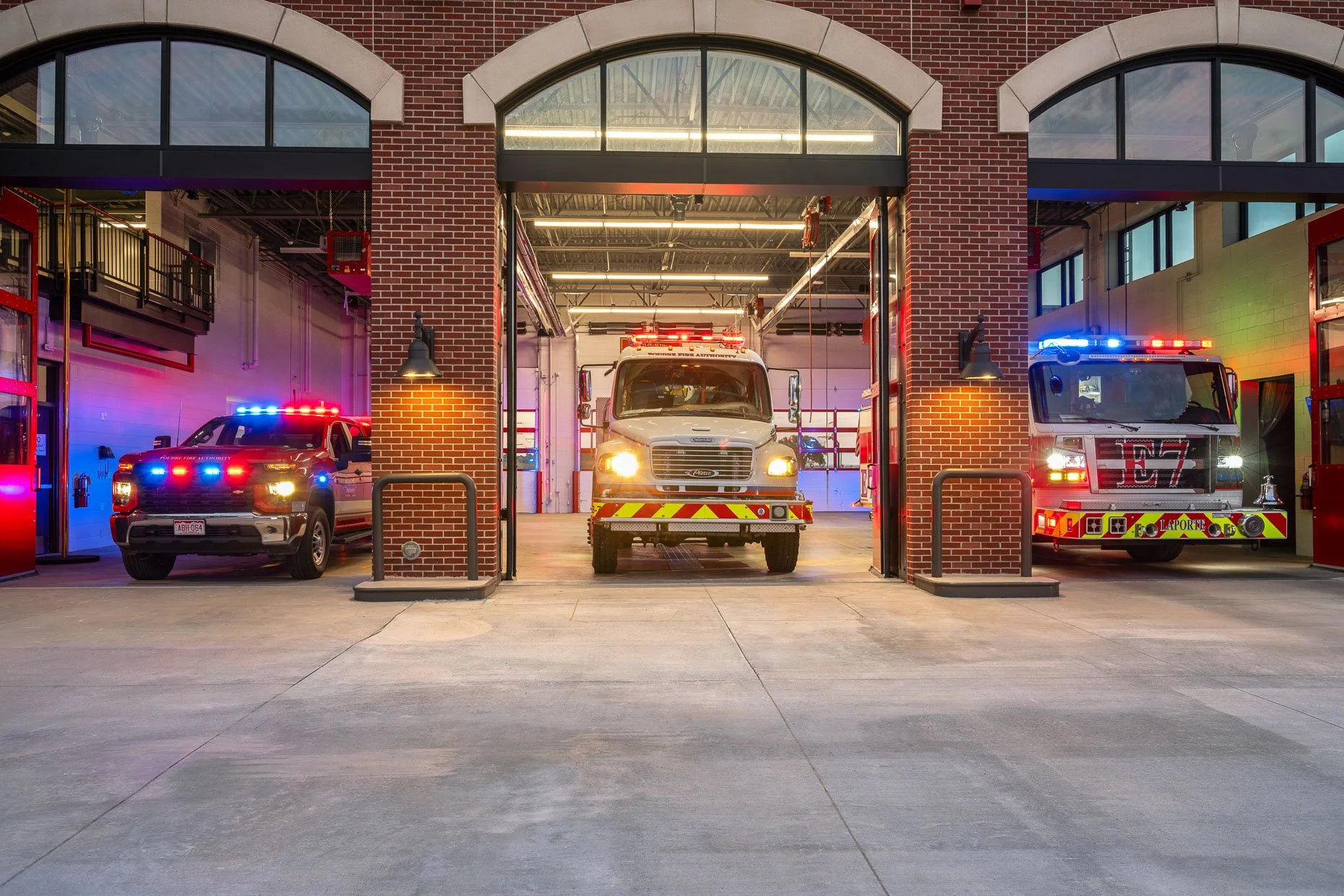 Fire station vehicle bays at dusk with lights on vehicles