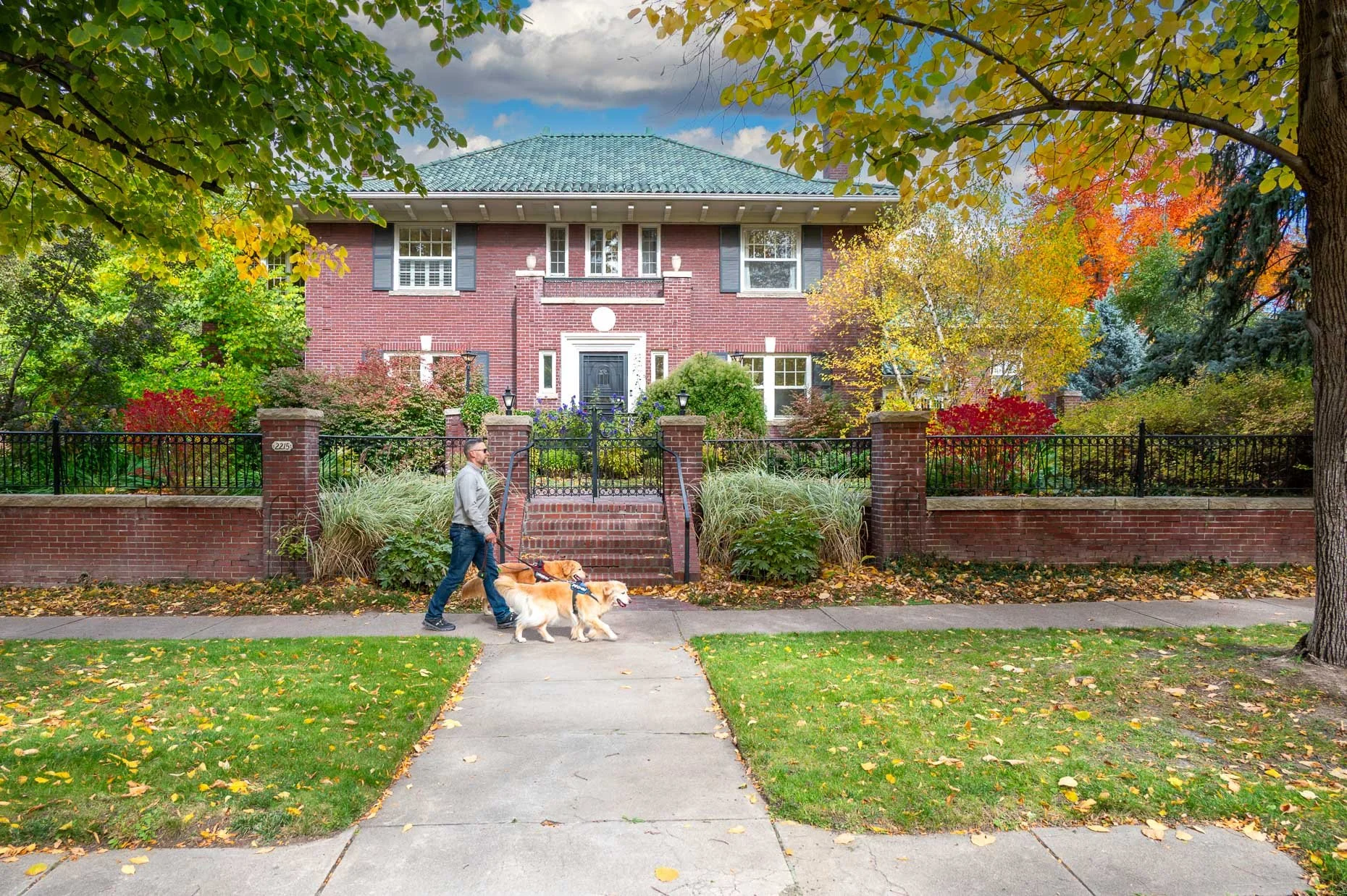 Front of home for sale on 7th Ave. Parkway in Denver with male walking two dogs in the fall.