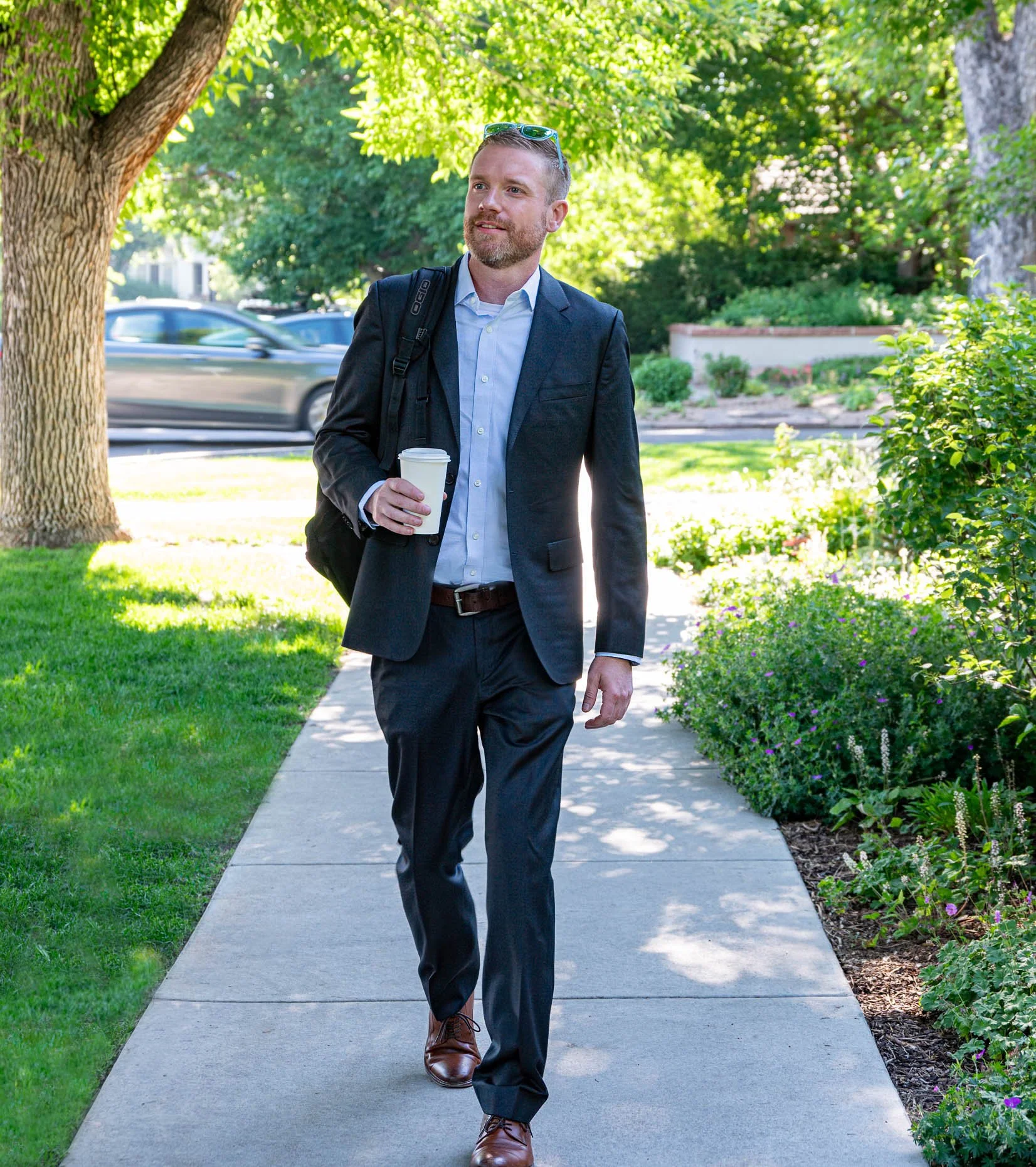 A man in a business suit walking on a sidewalk holding a cup of coffee.