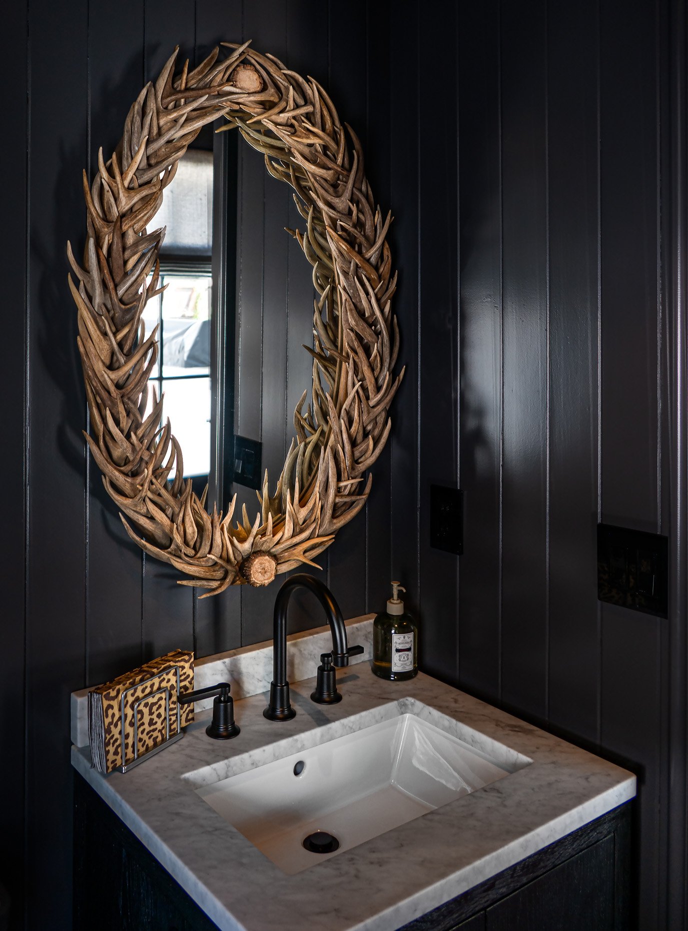 Dramatic powder room with antler mirror and marble sink