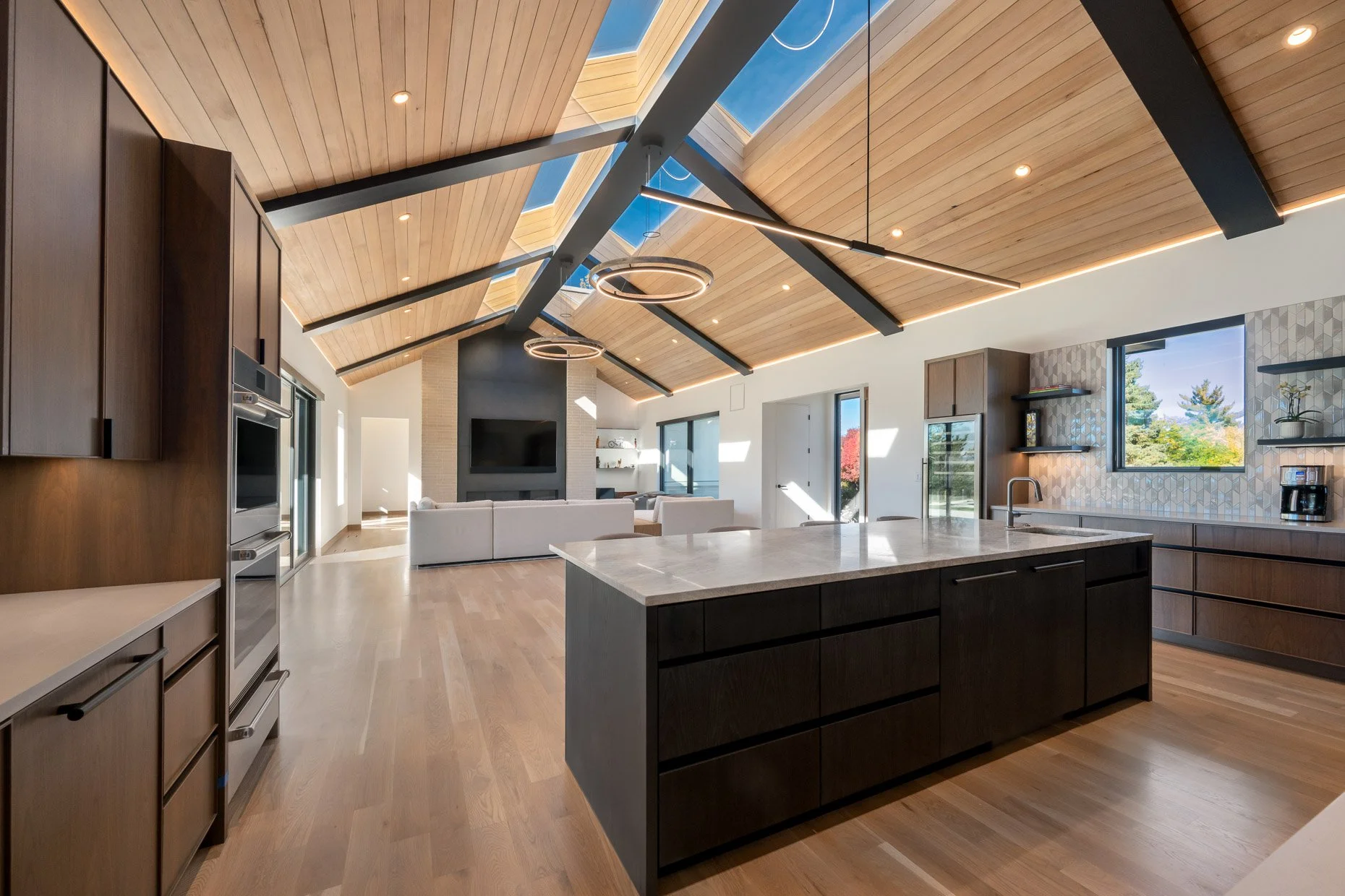 Design-build with open kitchen and family room, wood ceiling and skylights, center island, dark brown wood cabinetry and black iron ceiling design
