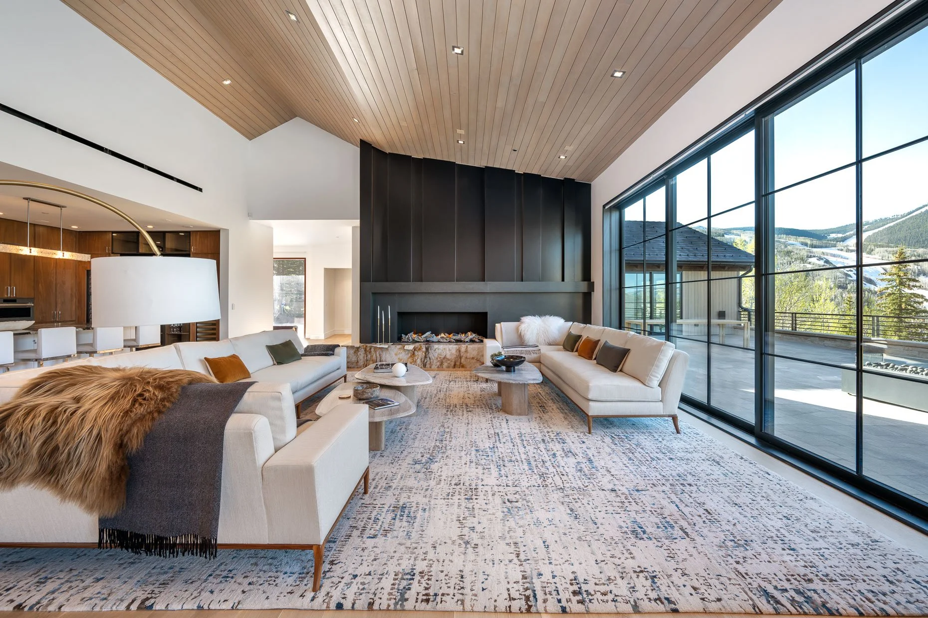 Large living room space with sculptured black fireplace, gorgeous plank wood ceilings and mountain views.