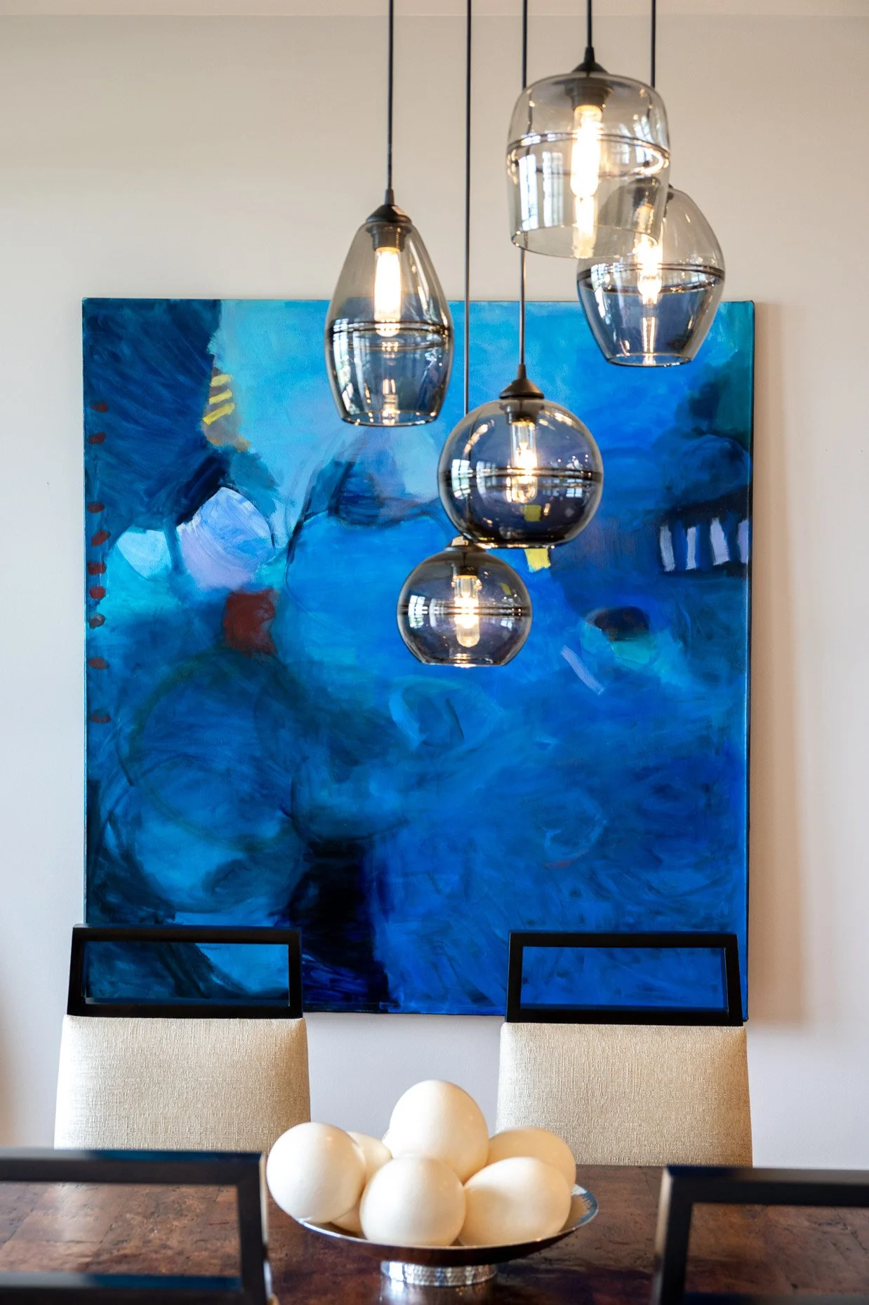 Dining room scene with dangling chandelier, gorgeous blue art, dining room chairs and centerpiece