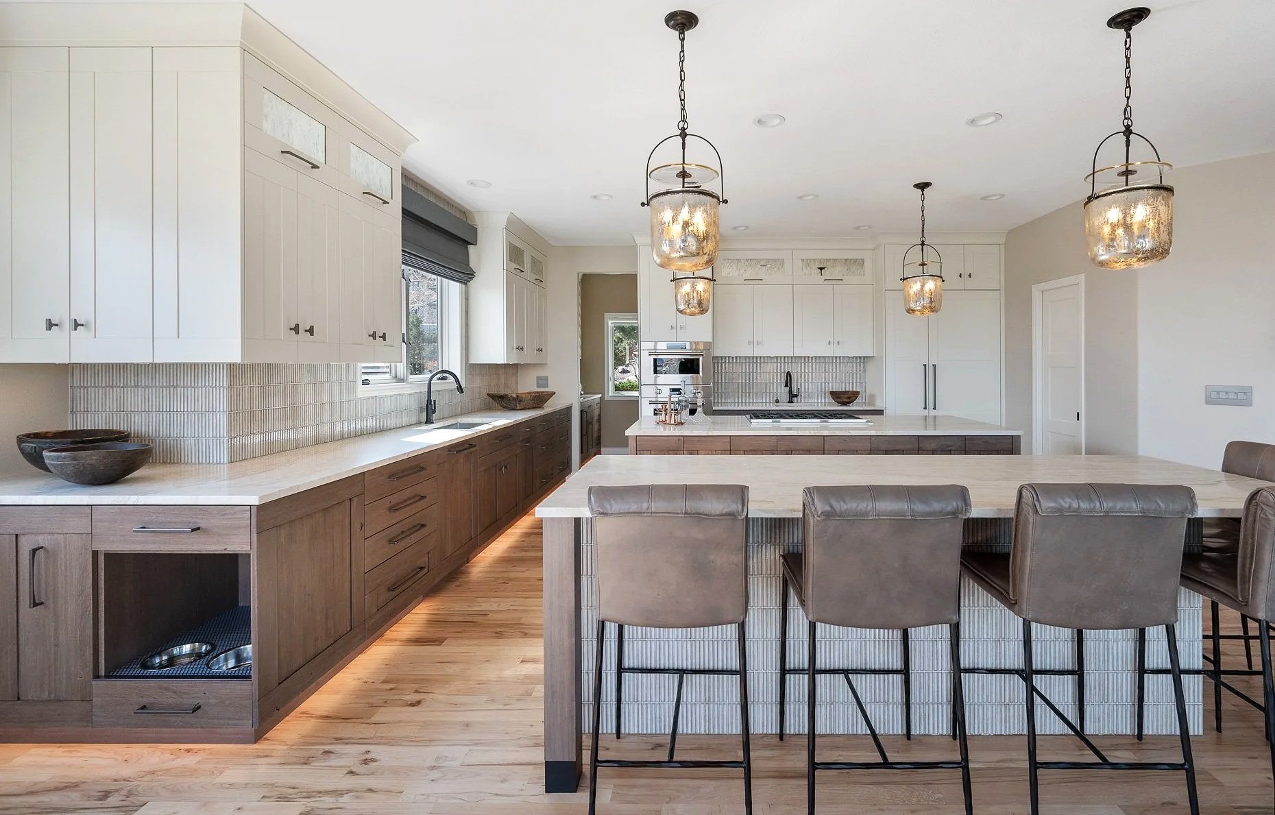 Large kitchen with two separate islands, space for dog bowls, designer tile backsplash, styled lighting, white and walnut cabinetry.