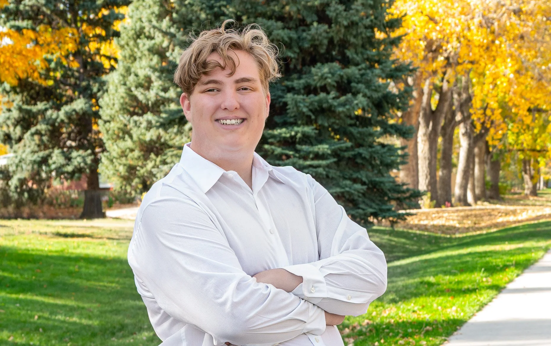 Senior boy in fall surroundings with white shirt and crossed arms.