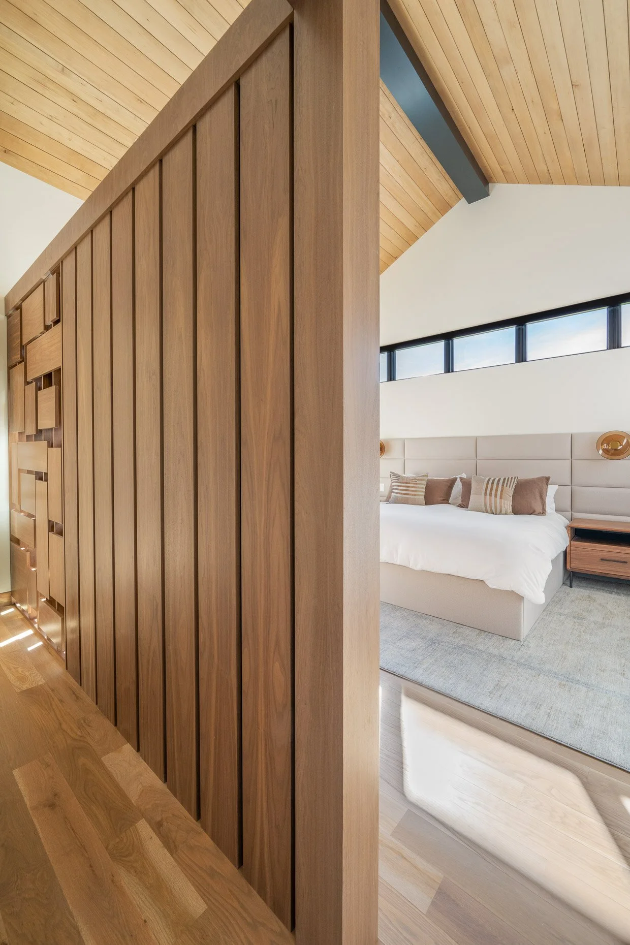 Custom designed wood wall entrance to spacious primary bedroom with wood panel walls and high window accents
