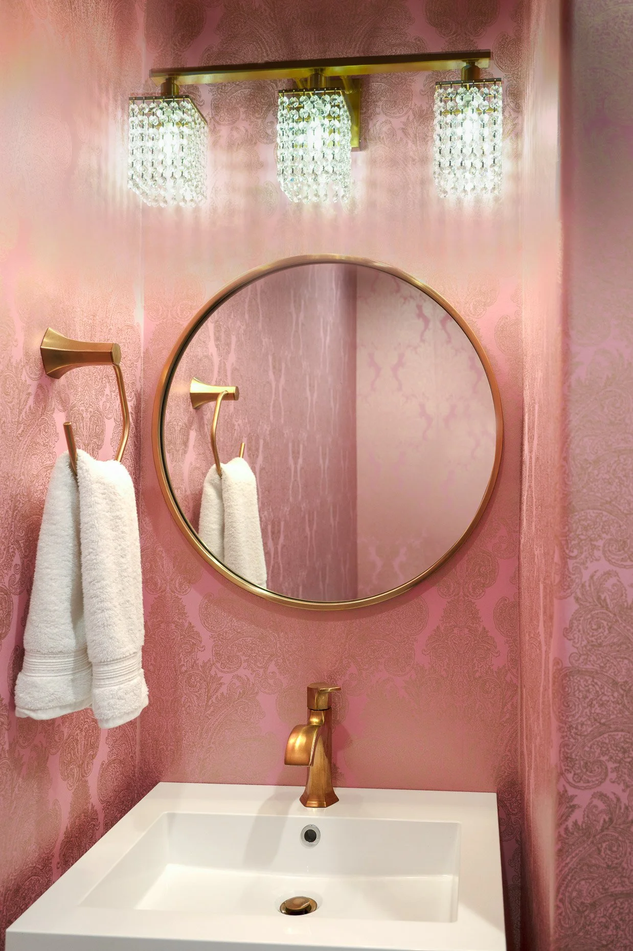 Pink wallpapered bathroom with gold fixtures and beautiful light accent