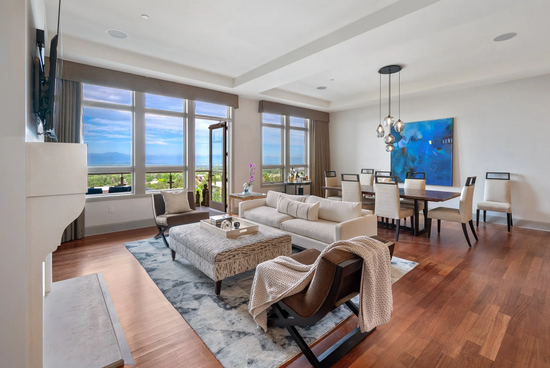 Modern living/dining room area with incredible mountain views, a large white fireplace and gorgeous wood floors
